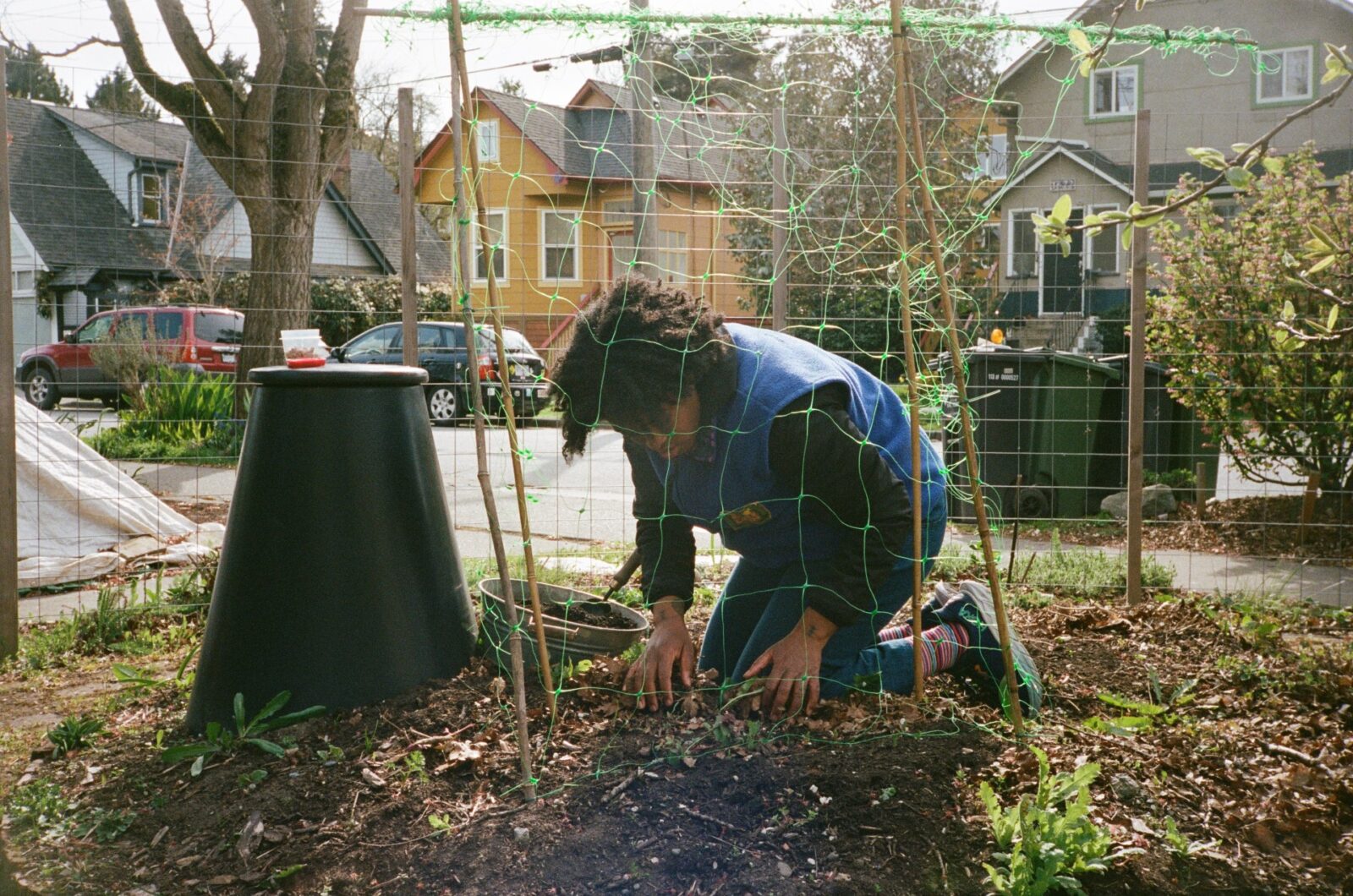 A C E C staff member is kneeling in a garden bed and riffling through a layer of dead leaves on top of the dirt.