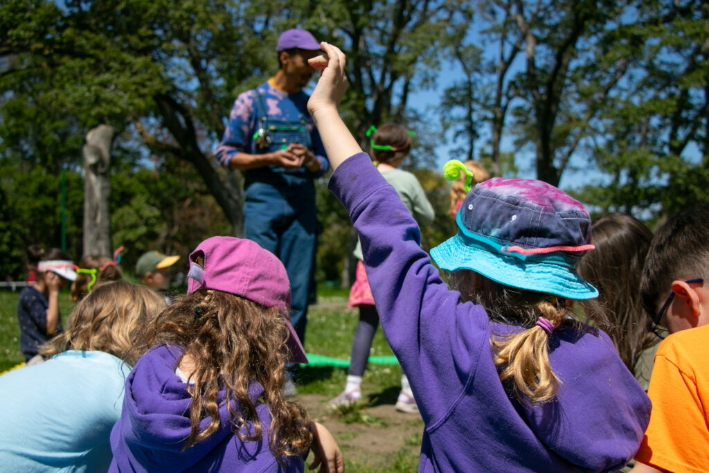 Children with their backs faced towards the camera are engaged in a lesson with the Child & Youth Education Coordinator.