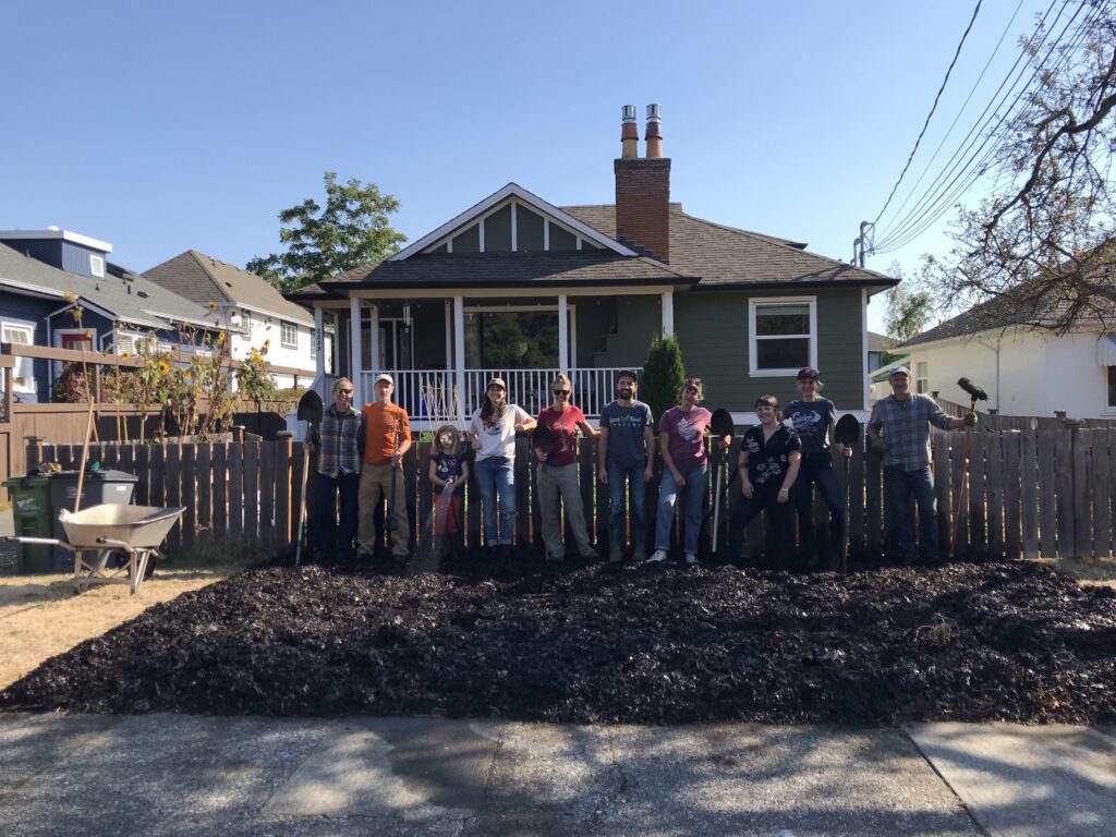 Sheet mulching workshop attendees standing in front of boulevard. a gray house is in the background.